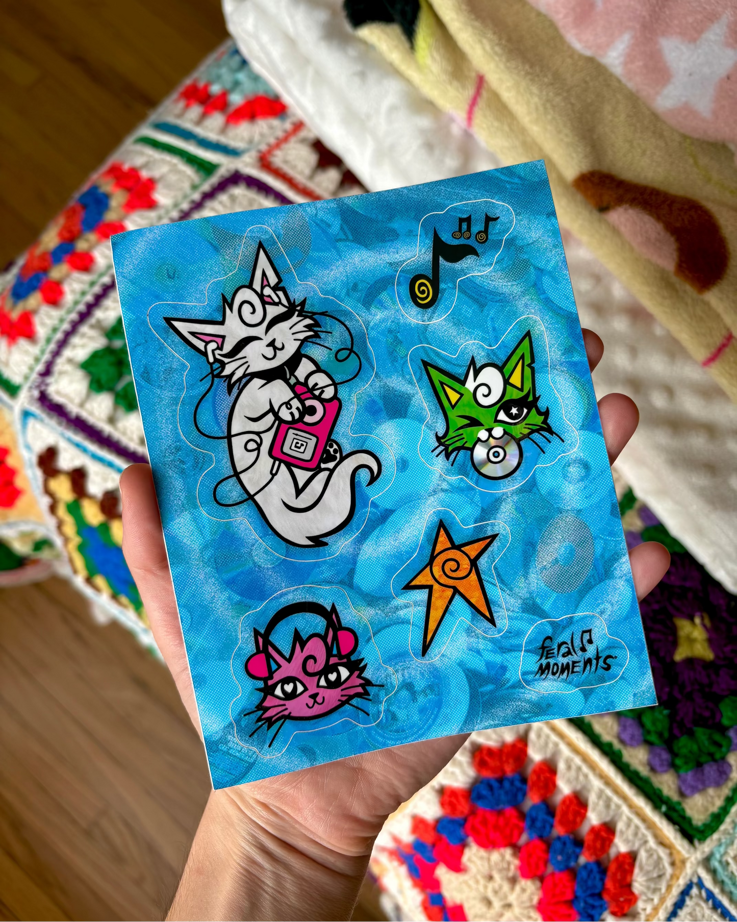 Hand holding a small blue sticker sheet with cartoon cat designs. 